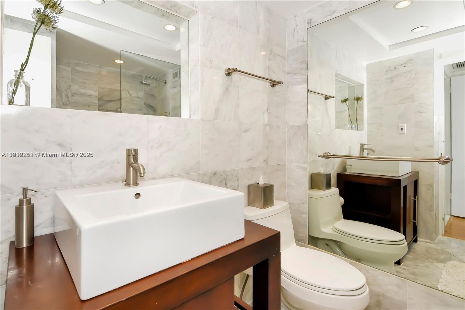 A modern bathroom features a white vessel sink, a toilet, and marble wall tiles — 5151 Collins Ave # 619, Miami Beach FL 33140, MIAMI BEACH, FL