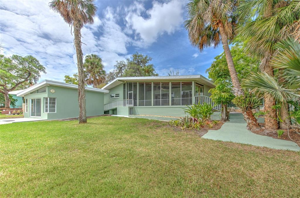 A green house with a screened-in porch and palm trees on a grassy lawn — 7102 MANDY LANE, NEW PORT RICHEY, FL