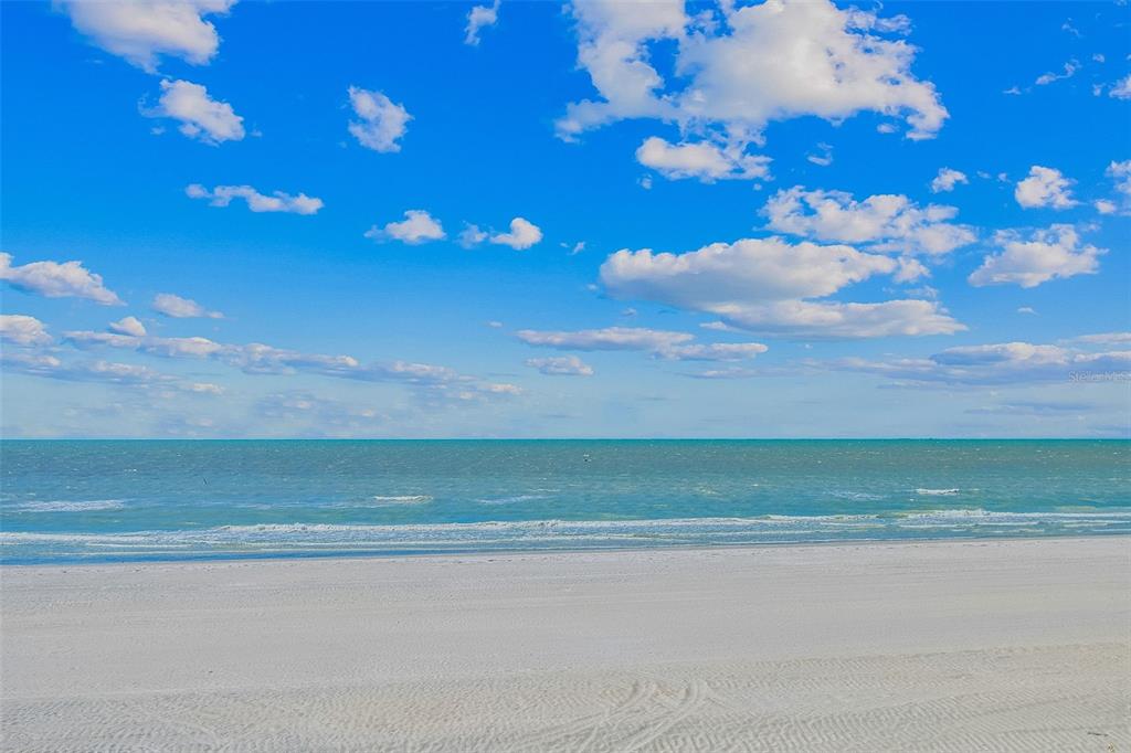 A wide, sandy beach meets the turquoise ocean under a bright blue, cloudy sky — 19710 GULF BOULEVARD UNIT 203, INDIAN SHORES, FL