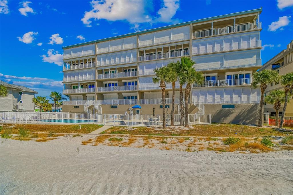 A multi-story beachfront condominium building features balconies, white shutters, and a ground-level swimming pool — 19710 GULF BOULEVARD UNIT 203, INDIAN SHORES, FL