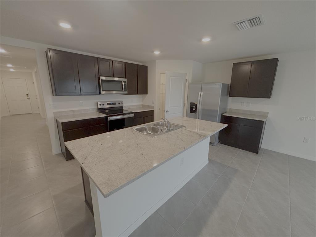 A kitchen features dark wood cabinets, light granite countertops, a center island, and stainless appliances — 481 W REXFORD DRIVE, BEVERLY HILLS, FL