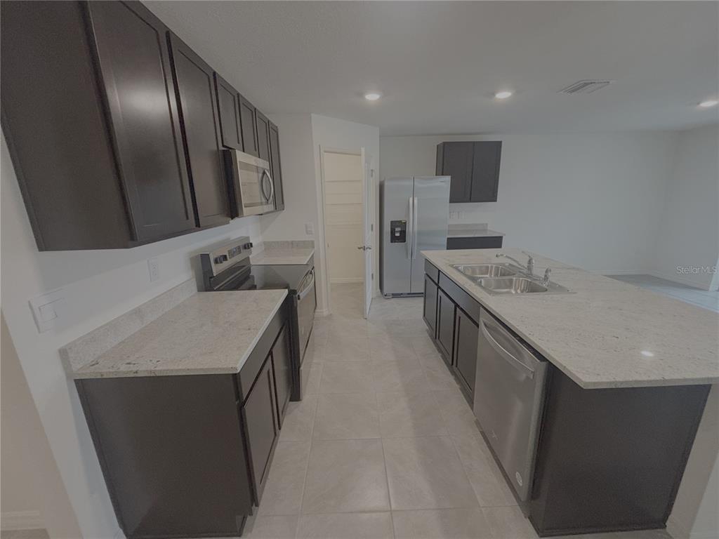 A kitchen features dark wood cabinets, light granite countertops, stainless steel appliances, and a central island — 481 W REXFORD DRIVE, BEVERLY HILLS, FL