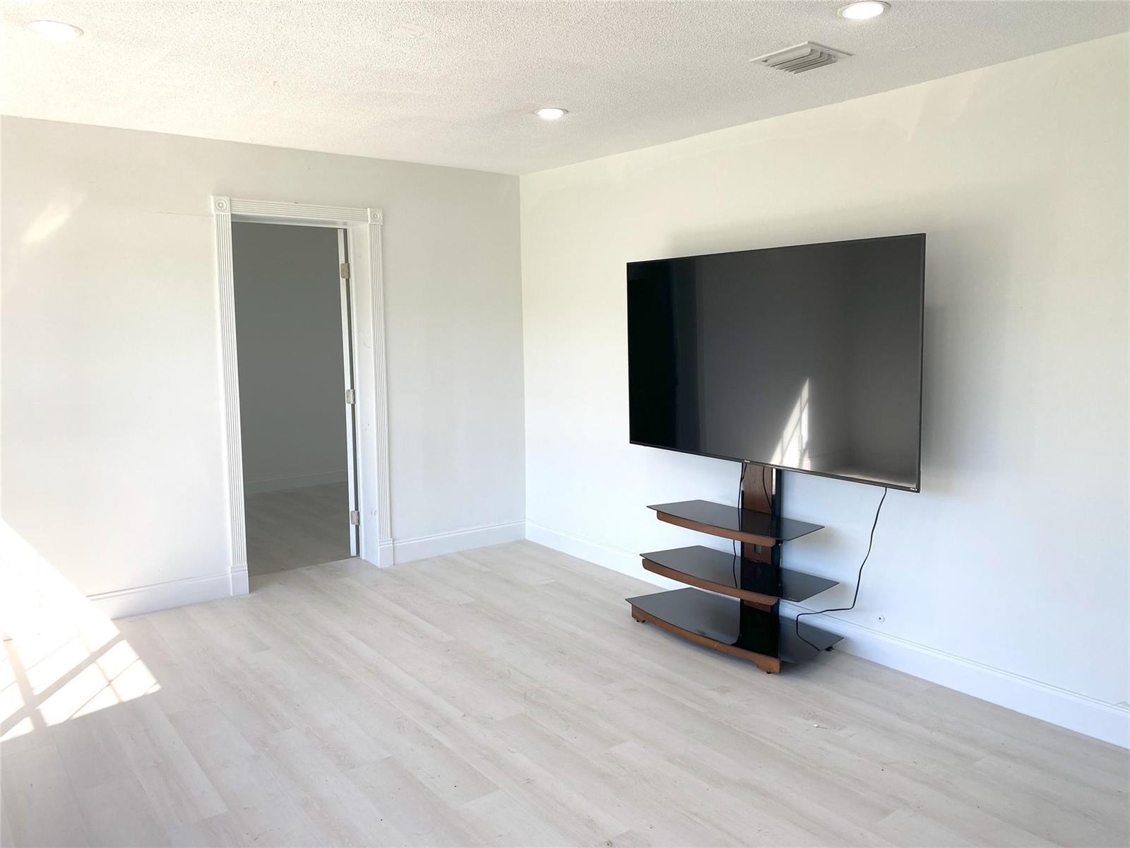 A bright room features light wood-look flooring, white walls, recessed lighting, and a wall-mounted television — 320 NW 4th Avenue # 1, Deerfield Beach FL 33441, DEERFIELD BEACH, FL