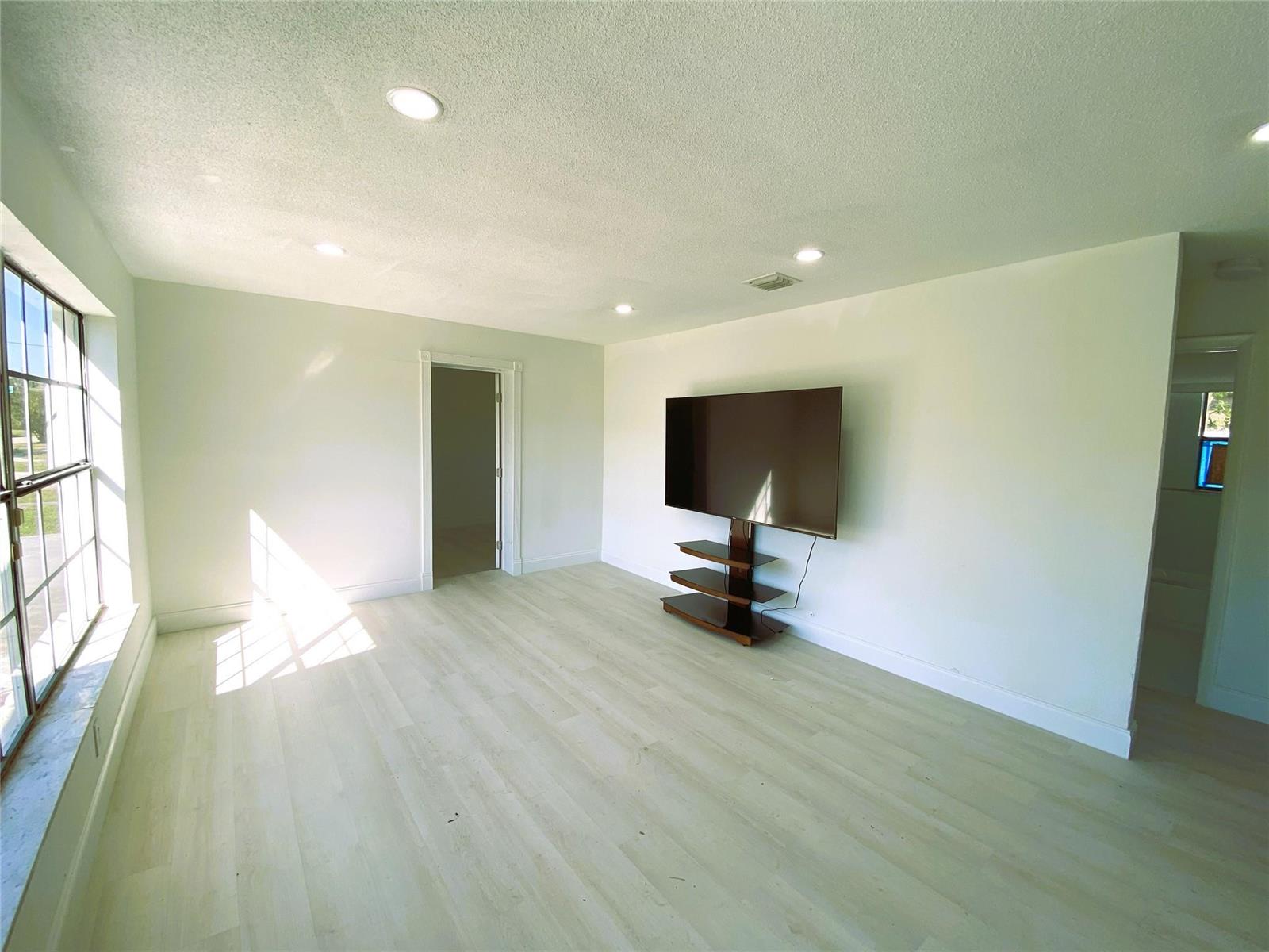 A bright room features light wood-look flooring, white walls, recessed lighting, and a wall-mounted television — 320 NW 4th Avenue # 1, Deerfield Beach FL 33441, DEERFIELD BEACH, FL