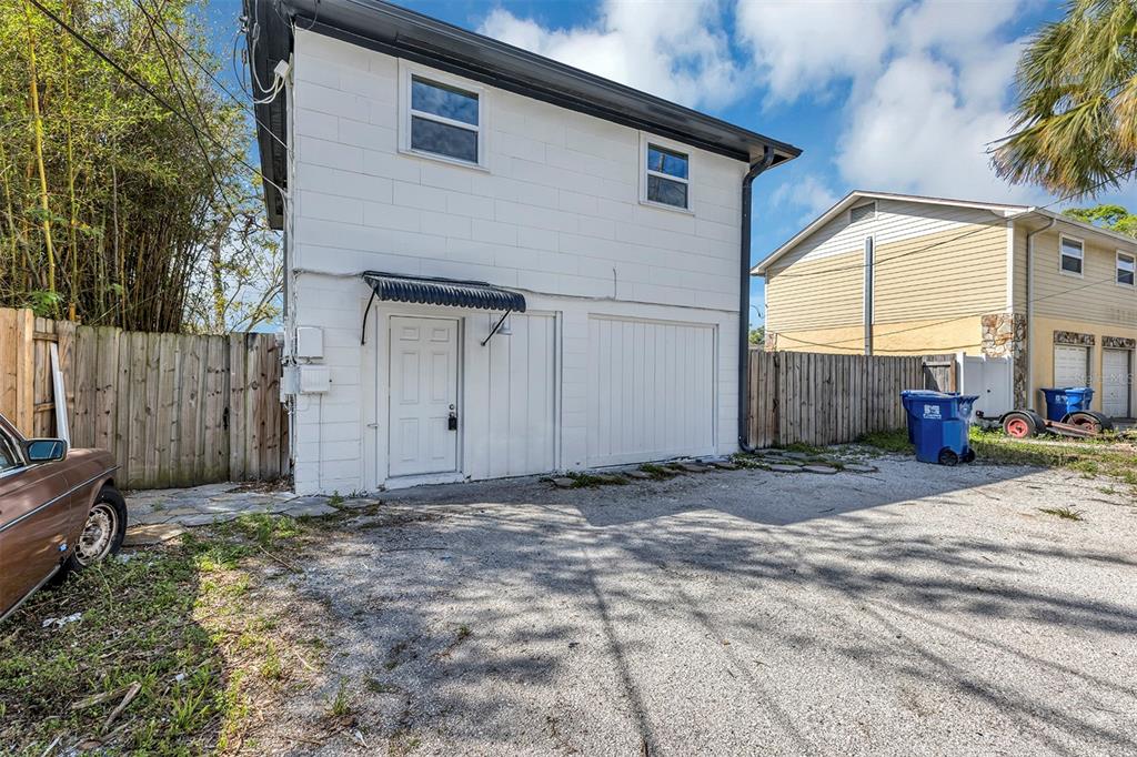 A two-story white concrete block building features a ground-level door and garage next to a gravel driveway — 2027 30TH AVENUE N Bottom unit, ST PETERSBURG, FL