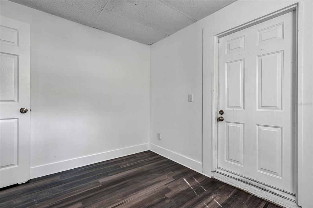 A room with white walls, dark wood-look flooring, a ceiling tile grid, and two doors — 2027 30TH AVENUE N Bottom unit, ST PETERSBURG, FL