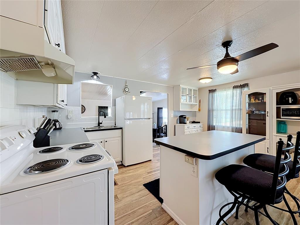 A kitchen features white cabinetry, a white stove, a refrigerator, and a central island — 1025 CAPELLA DRIVE, TAVARES, FL