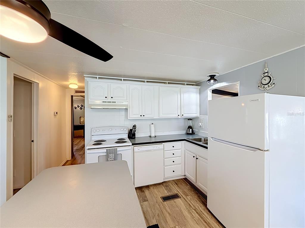 A kitchen features white cabinets, a white refrigerator, a stove, and wood-look flooring — 1025 CAPELLA DRIVE, TAVARES, FL
