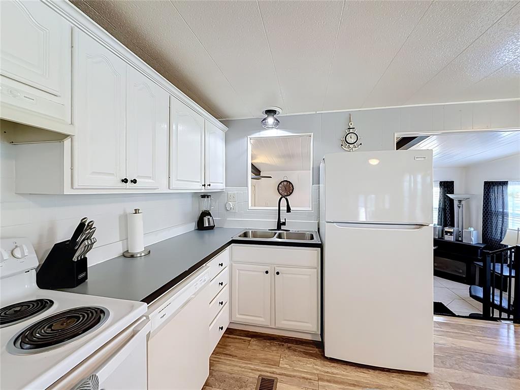 A kitchen features white cabinets, dark countertops, a white refrigerator, and a sink — 1025 CAPELLA DRIVE, TAVARES, FL
