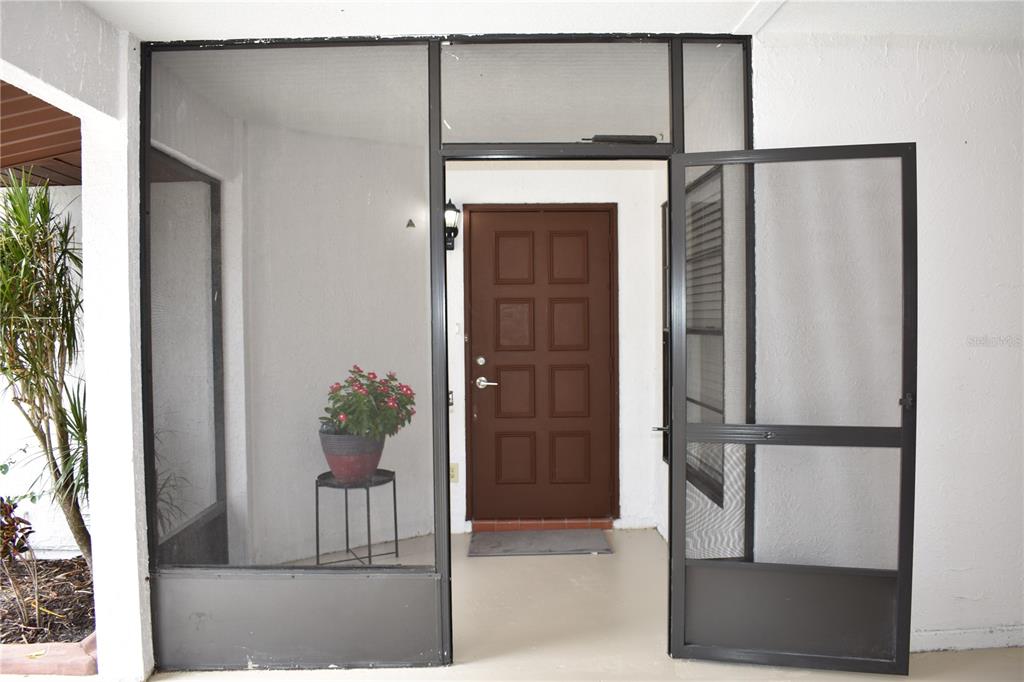 A brown front door is visible behind a black-framed screen door and enclosure — 1702 AURA COURT, SUN CITY CENTER, FL