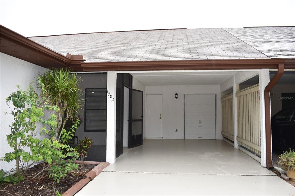 A covered carport with a white door and a screened-in entryway at a residential home — 1702 AURA COURT, SUN CITY CENTER, FL
