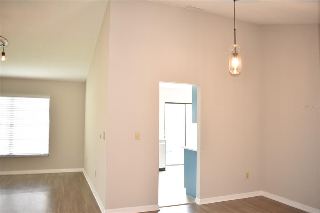 A view of a room with light-colored walls, wood-look flooring, and a doorway to a kitchen — 1702 AURA COURT, SUN CITY CENTER, FL