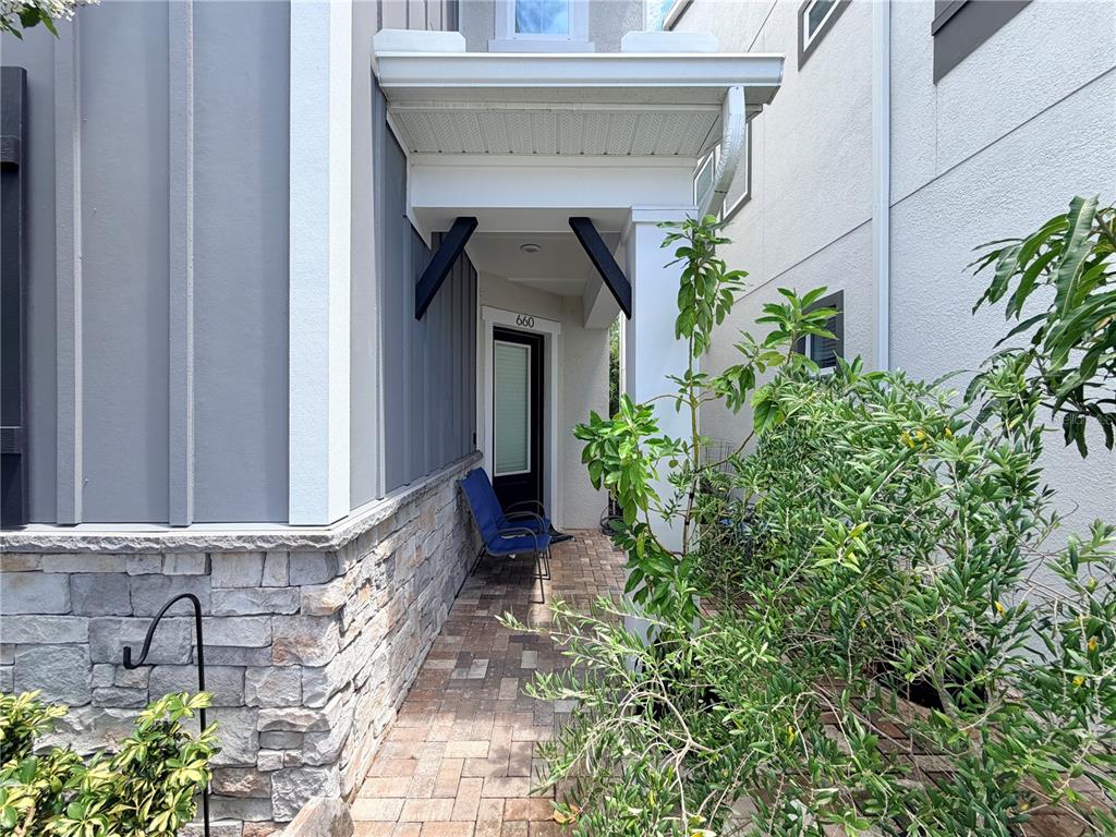 A paved walkway leads to a covered entryway with stone siding and a blue chair — 660 ROSEWOOD WAY, LAKE MARY, FL