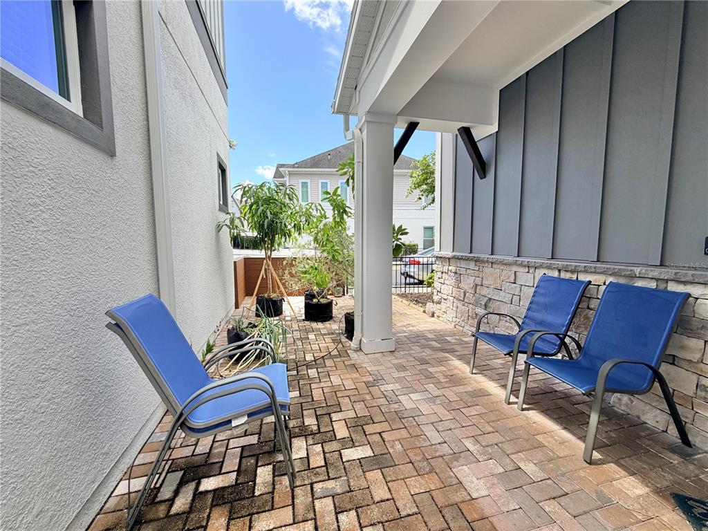 A paved patio features three blue chairs and several potted plants under a covered porch — 660 ROSEWOOD WAY, LAKE MARY, FL