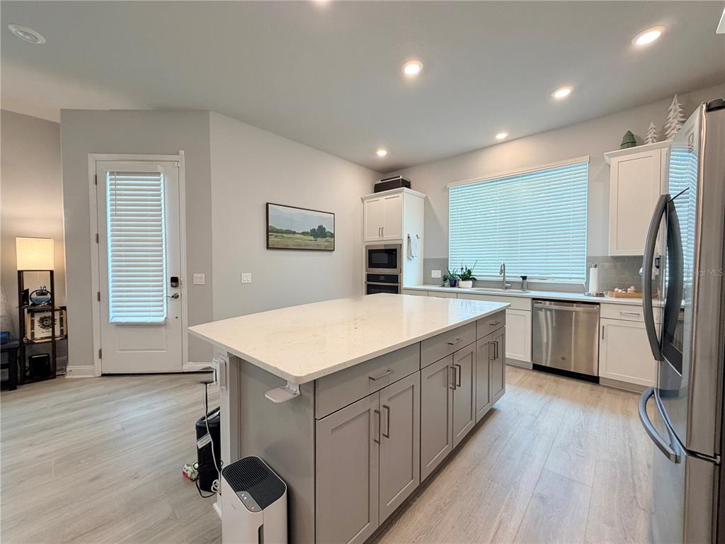 A modern kitchen features a gray island, white cabinetry, stainless steel appliances, and light flooring — 660 ROSEWOOD WAY, LAKE MARY, FL
