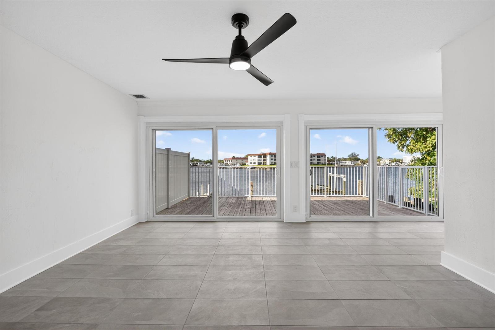 An empty room with gray tile flooring, a ceiling fan, and sliding doors overlooking water — 624 Southwind Circle # 3, North Palm Beach FL 33408, NORTH PALM BEACH, FL