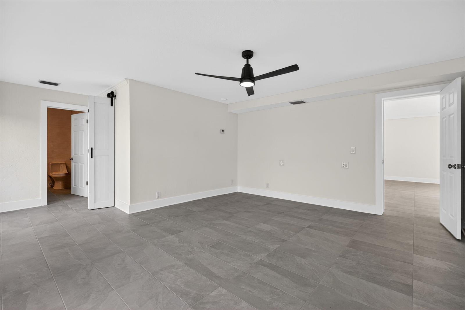 A room with gray tile flooring, a black ceiling fan, and two open doorways — 624 Southwind Circle # 3, North Palm Beach FL 33408, NORTH PALM BEACH, FL