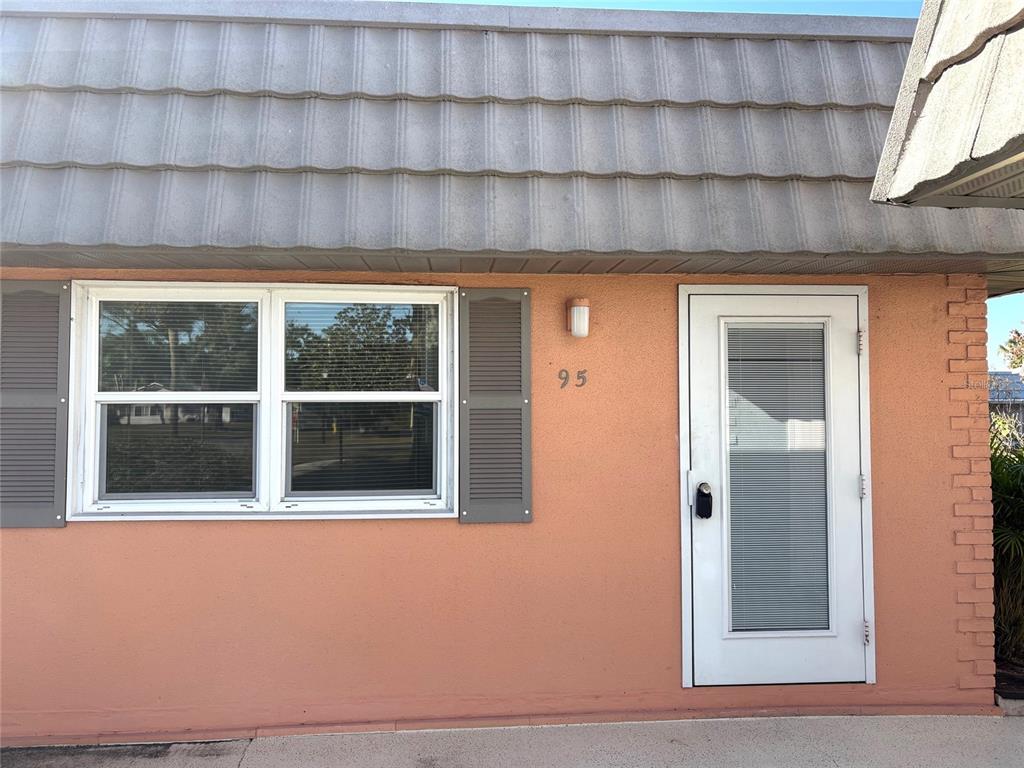 The exterior of a peach-colored building features a white door, a window with shutters, and a tiled roof — 201 BEDFORD STREET UNIT 95, SUN CITY CENTER, FL