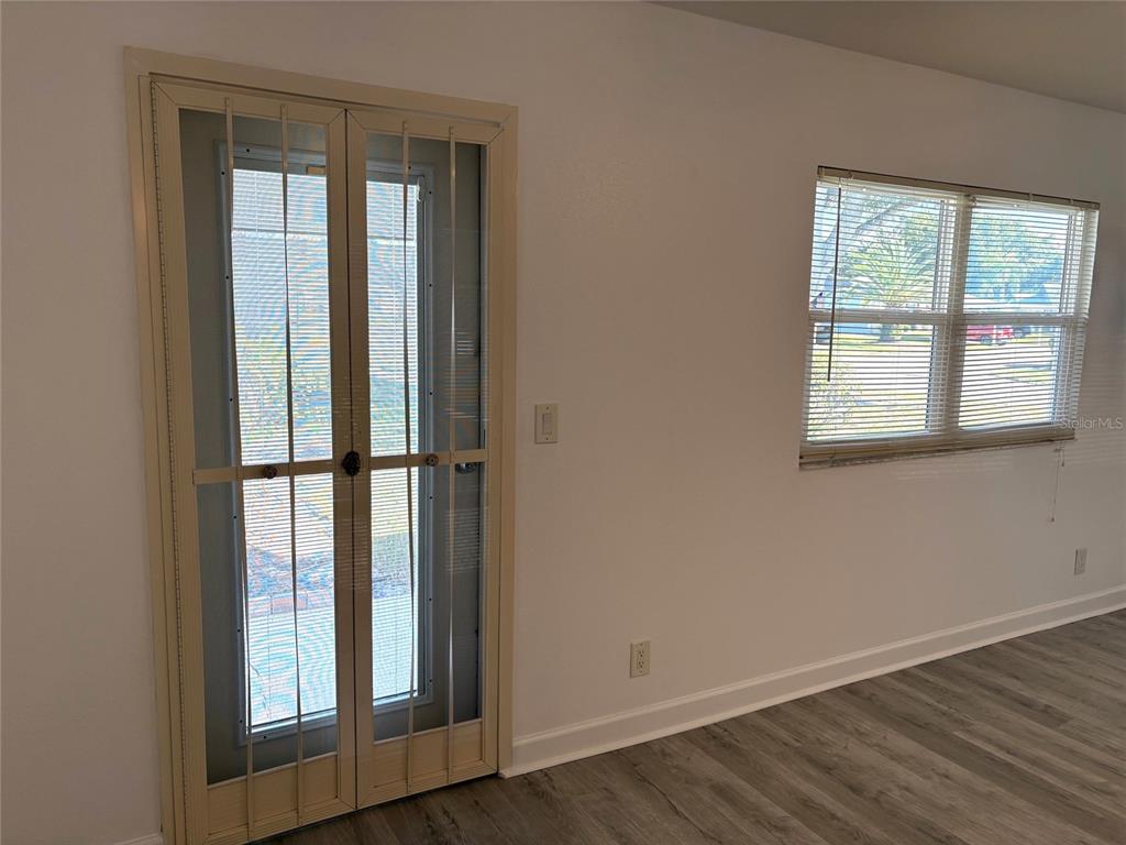 A room with light-colored walls, wood-look flooring, a window with blinds, and a screen door — 201 BEDFORD STREET UNIT 95, SUN CITY CENTER, FL