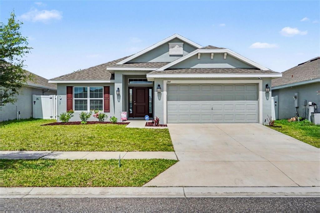 A single-story suburban house with a gray stucco exterior, a two-car garage, and red shutters — 284 CITRUS POINTE DRIVE, HAINES CITY, FL