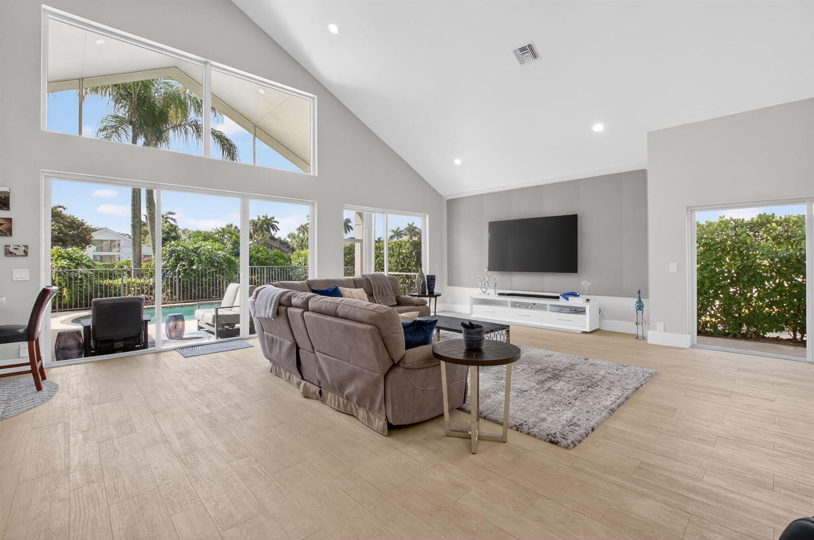 A spacious living room features vaulted ceilings, light wood-look tile floors, and large sliding doors — 17320 Loch Lomond Way, Boca Raton FL 33496, BOCA RATON, FL