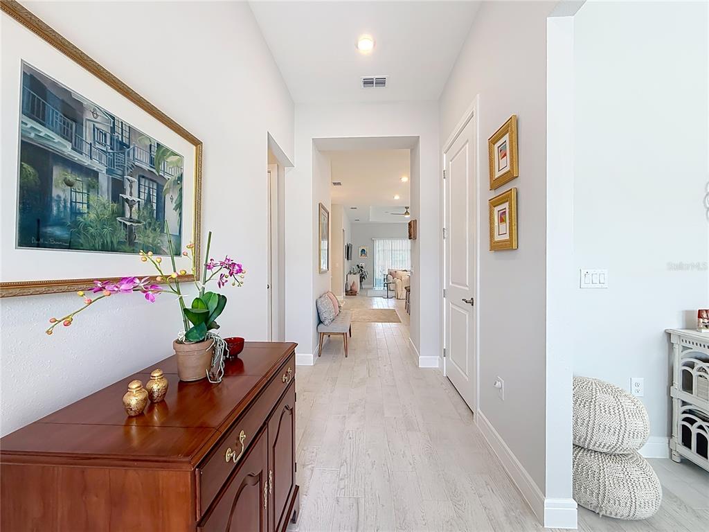 A hallway with light wood-look flooring leads from a foreground console table toward a living area — 9027 SW 52ND PLACE ROAD, OCALA, FL