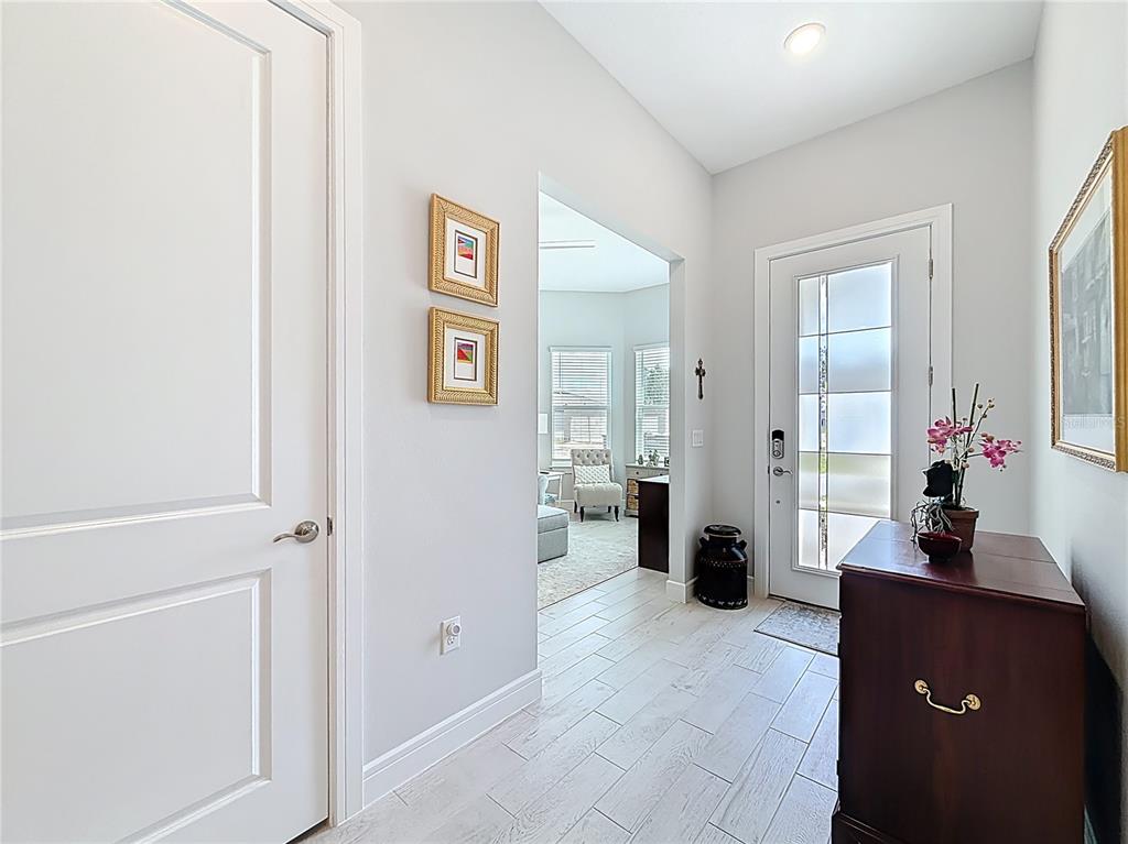 A bright entryway features light wood-look tile flooring, a white front door, and a wooden console — 9027 SW 52ND PLACE ROAD, OCALA, FL