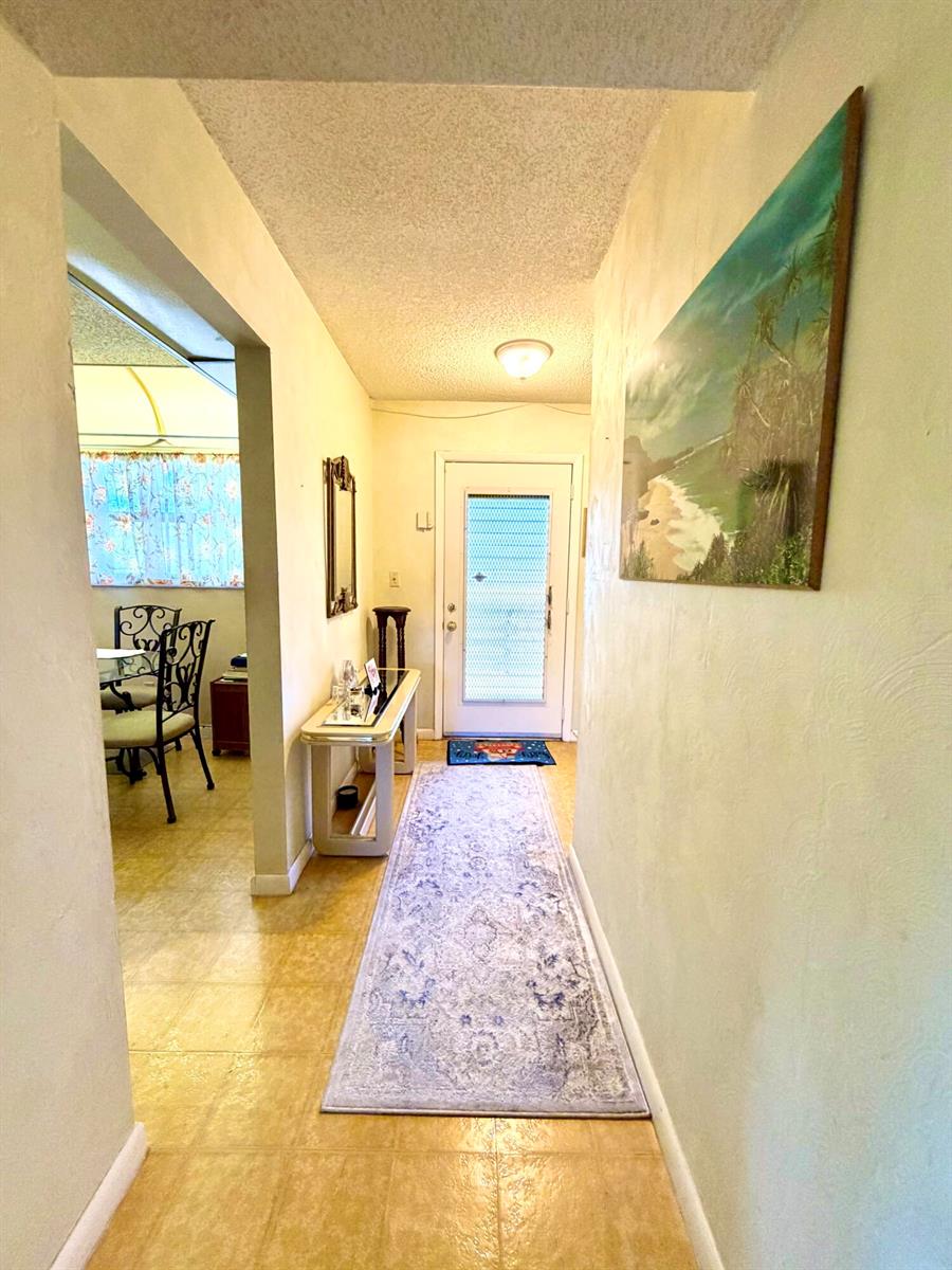 A hallway with a runner rug leads to a front door, with a dining area visible — 4970 E Sabal Palm Boulevard # 315, Tamarac FL 33319, TAMARAC, FL