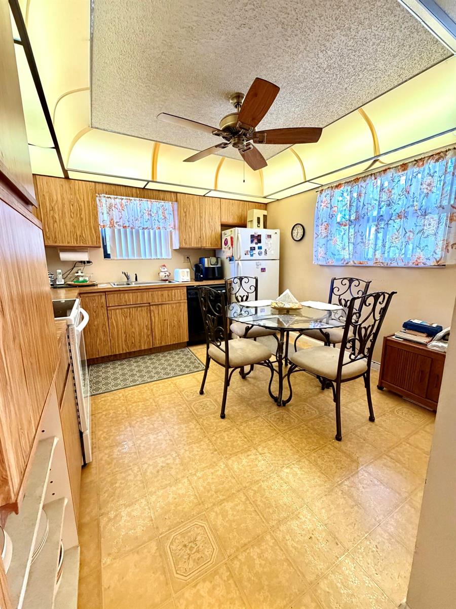 A kitchen with wood cabinets, a dining table, and a ceiling fan over vinyl flooring — 4970 E Sabal Palm Boulevard # 315, Tamarac FL 33319, TAMARAC, FL