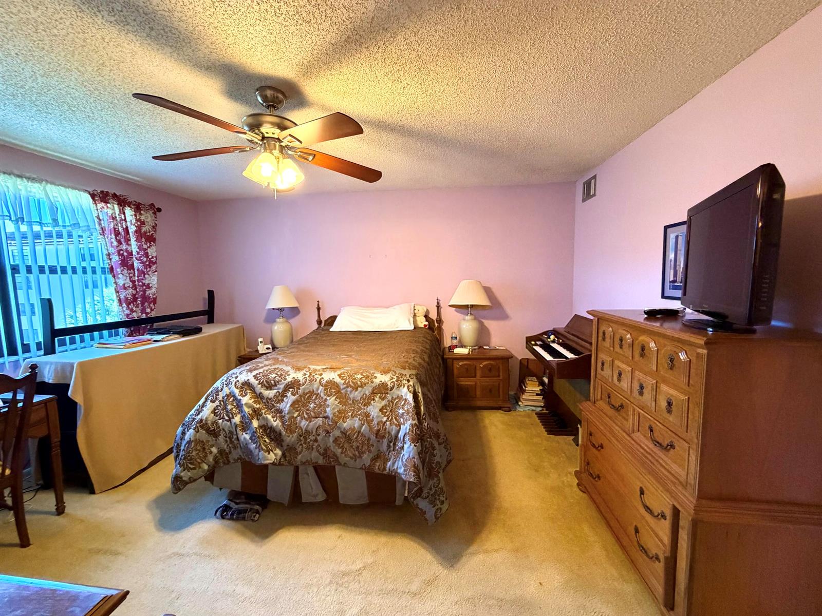 A bedroom features a bed, wooden dresser, ceiling fan, and a small organ on carpet — 4970 E Sabal Palm Boulevard # 315, Tamarac FL 33319, TAMARAC, FL