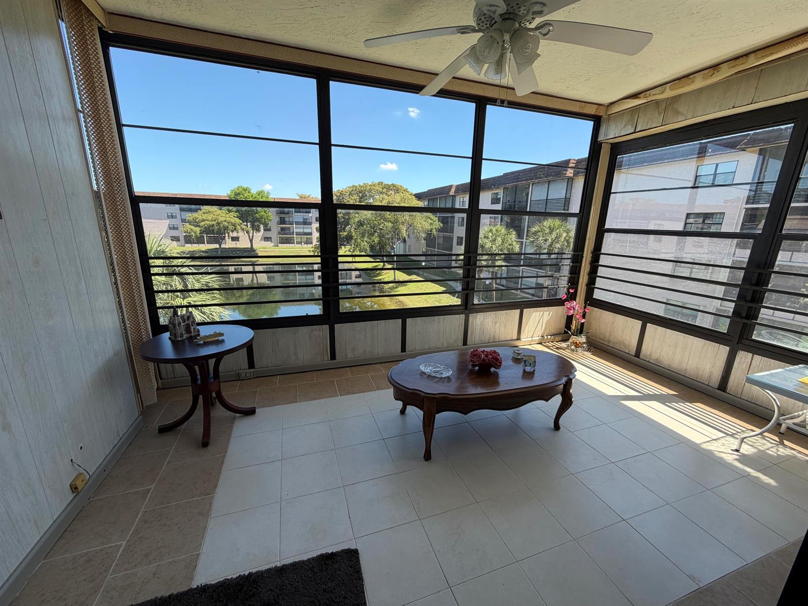 A sunroom with tile flooring, a ceiling fan, and large windows overlooking a pond and buildings — 4970 E Sabal Palm Boulevard # 315, Tamarac FL 33319, TAMARAC, FL