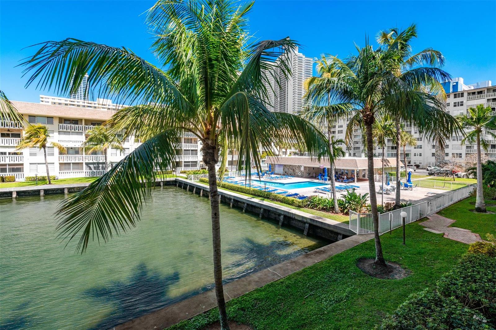 A view of a canal, a swimming pool, and palm trees beside a residential building — 1891 S Ocean Drive # 207, Hallandale Beach FL 33009, HALLANDALE BEACH, FL