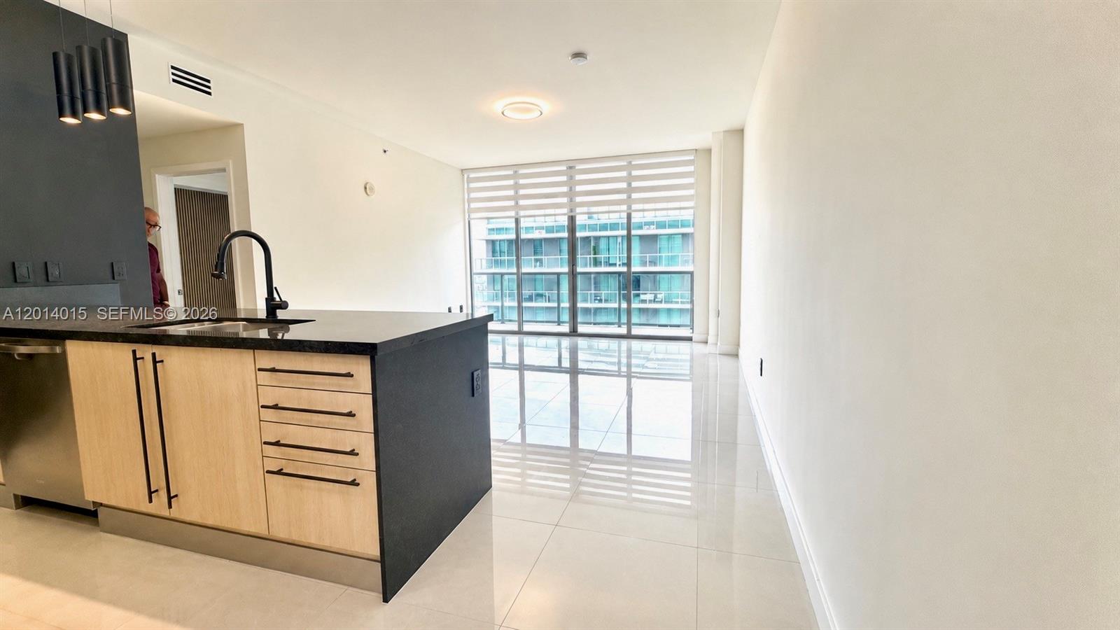 A modern kitchen island with light wood cabinets and black countertops faces a bright living area — 79 SW 12th St # 4008S, Miami FL 33130, MIAMI, FL