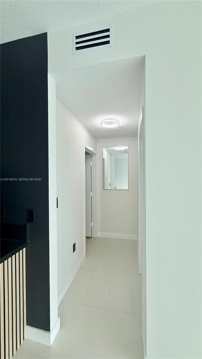 A hallway with light tile flooring leads to a doorway and a wall mirror — 79 SW 12th St # 4008S, Miami FL 33130, MIAMI, FL