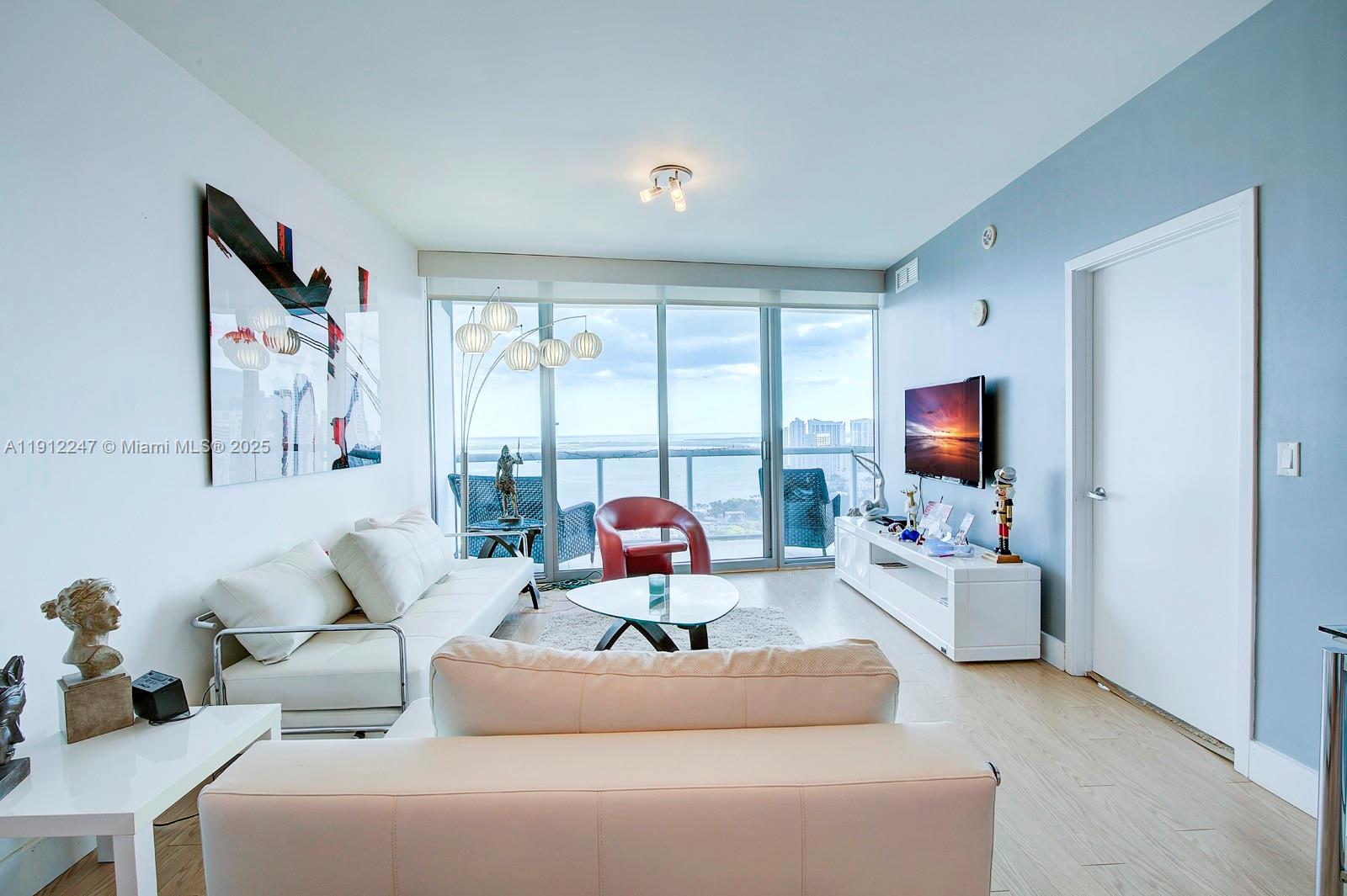 A living room features white sofas, a glass coffee table, and floor-to-ceiling windows with views — 888 Biscayne Blvd # 4007, Miami FL 33132, MIAMI, FL