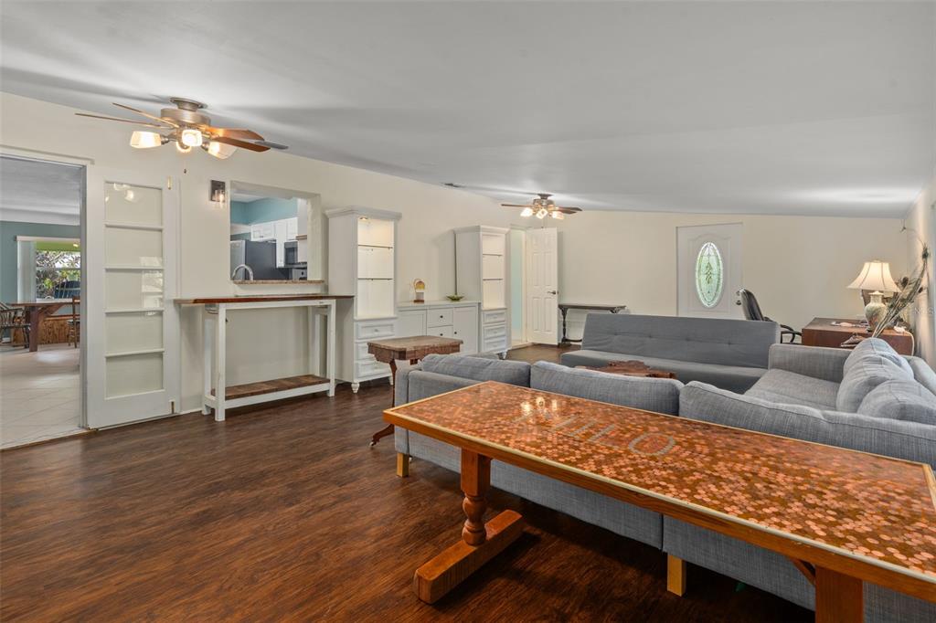 A living room features dark wood-look flooring, gray sectional sofas, and a penny-topped console table — 9812 51ST AVENUE N, ST PETERSBURG, FL