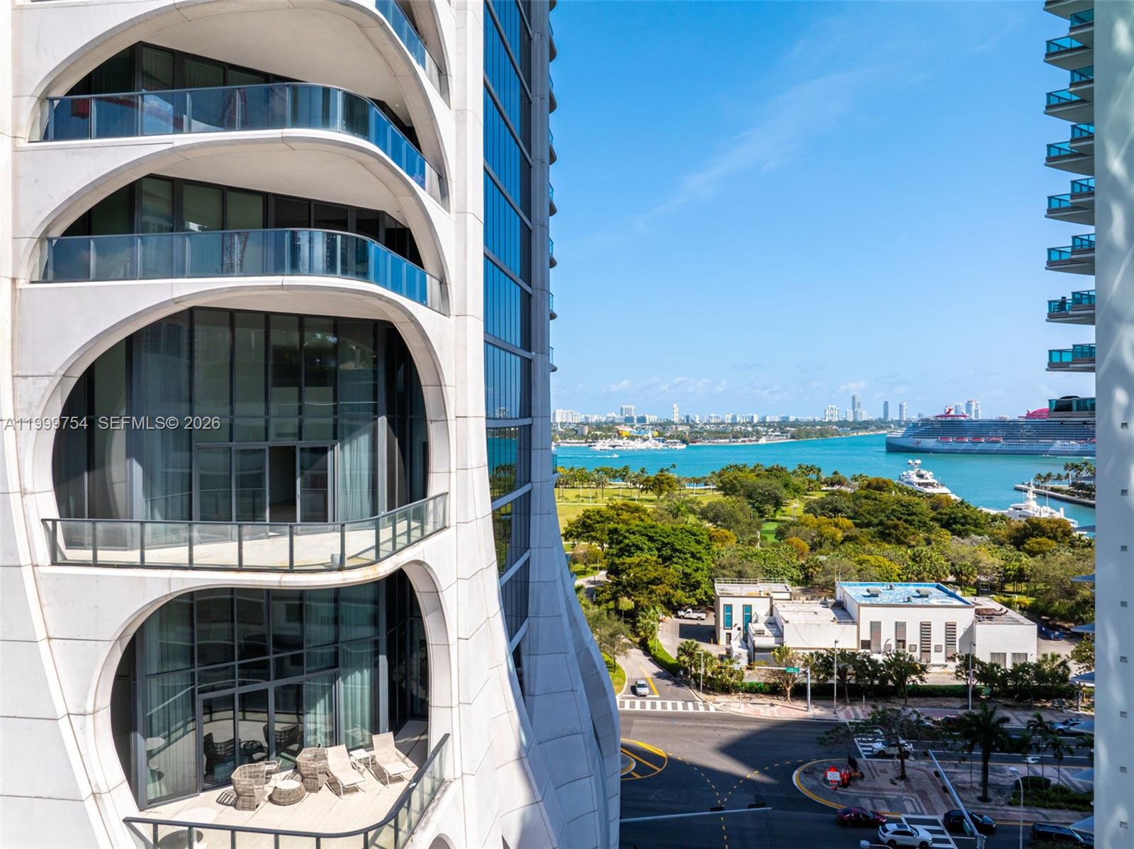 An exterior view shows a modern high-rise building with curved balconies overlooking a coastal park — 1000 Biscayne Blvd # 1201, Miami FL 33132, MIAMI, FL
