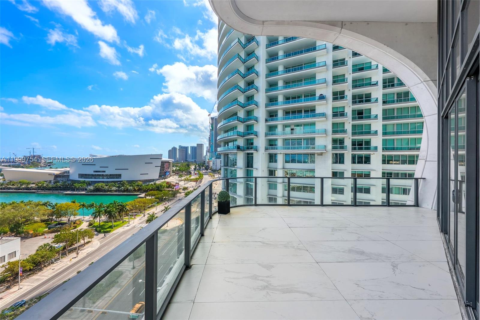A spacious balcony with white marble-look tile flooring overlooks a city skyline and waterfront — 1000 Biscayne Blvd # 1201, Miami FL 33132, MIAMI, FL
