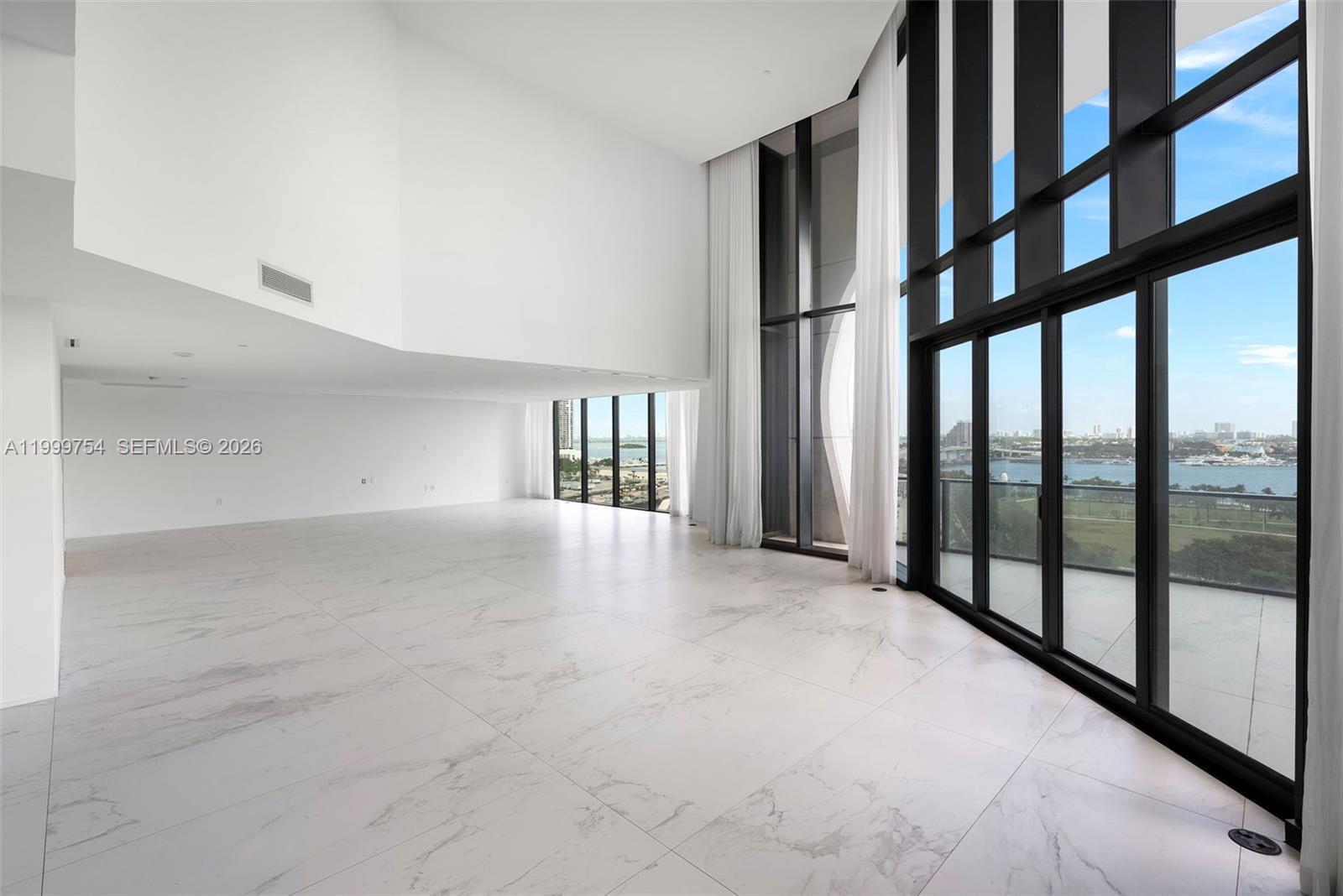 A spacious, minimalist living room features white marble floors, double-height ceilings, and floor-to-ceiling windows — 1000 Biscayne Blvd # 1201, Miami FL 33132, MIAMI, FL