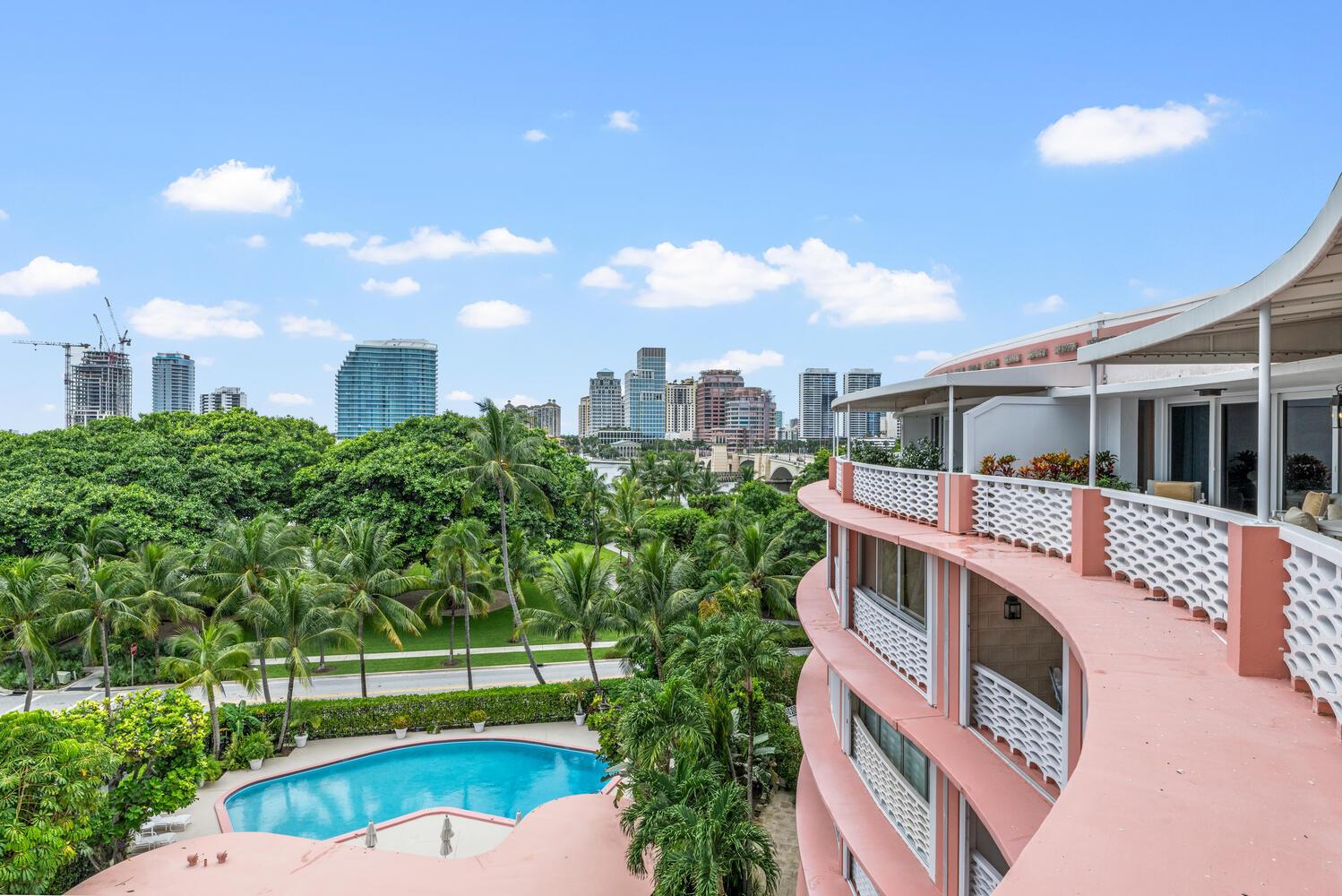 An elevated view of a curved pink balcony overlooking a swimming pool and city skyline — 315 S Lake Drive # C, Palm Beach FL 33480, PALM BEACH, FL