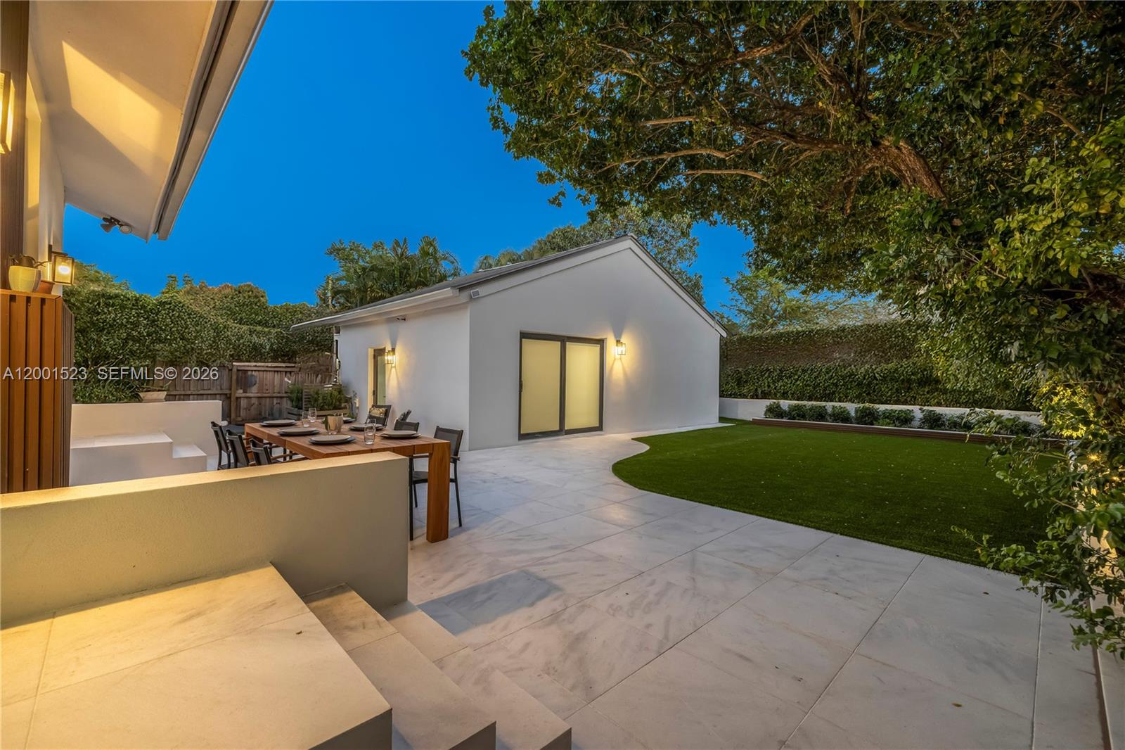 A patio with a dining table and artificial grass lawn sits before a detached building — 320 NE 88th St, El Portal FL 33138, EL PORTAL, FL