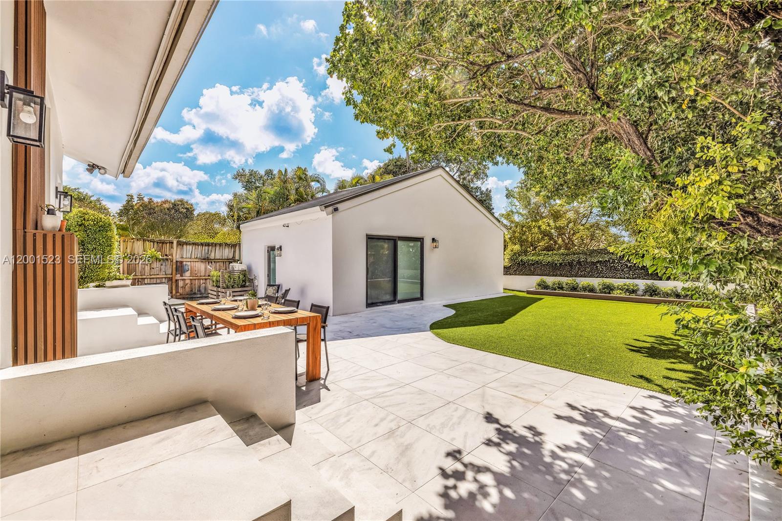 A backyard patio features a wooden dining table, white tile flooring, and a grassy lawn — 320 NE 88th St, El Portal FL 33138, EL PORTAL, FL