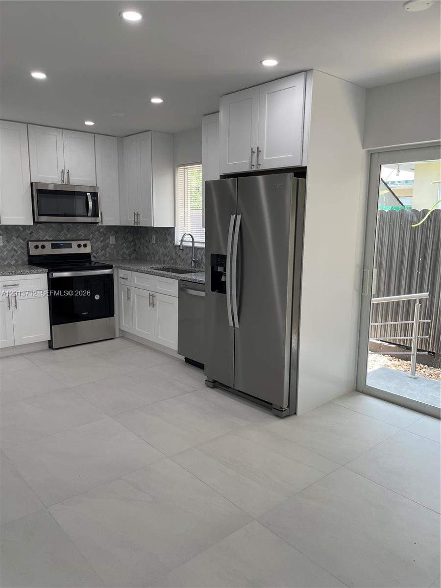 A modern kitchen features white cabinets, stainless steel appliances, gray tile flooring, and a glass door — 6820 SW 13th Ter # 6820, Miami FL 33144, MIAMI, FL