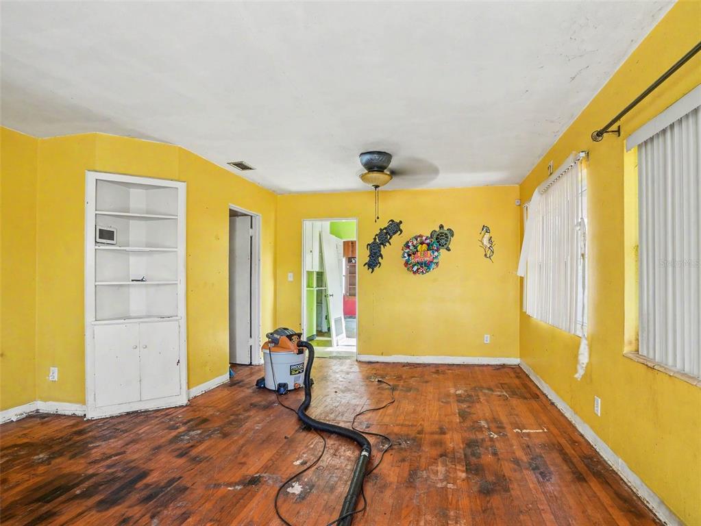 An empty room with yellow walls, hardwood floors, a built-in shelf, and a ceiling fan — 2207 AVENUE B NW, WINTER HAVEN, FL