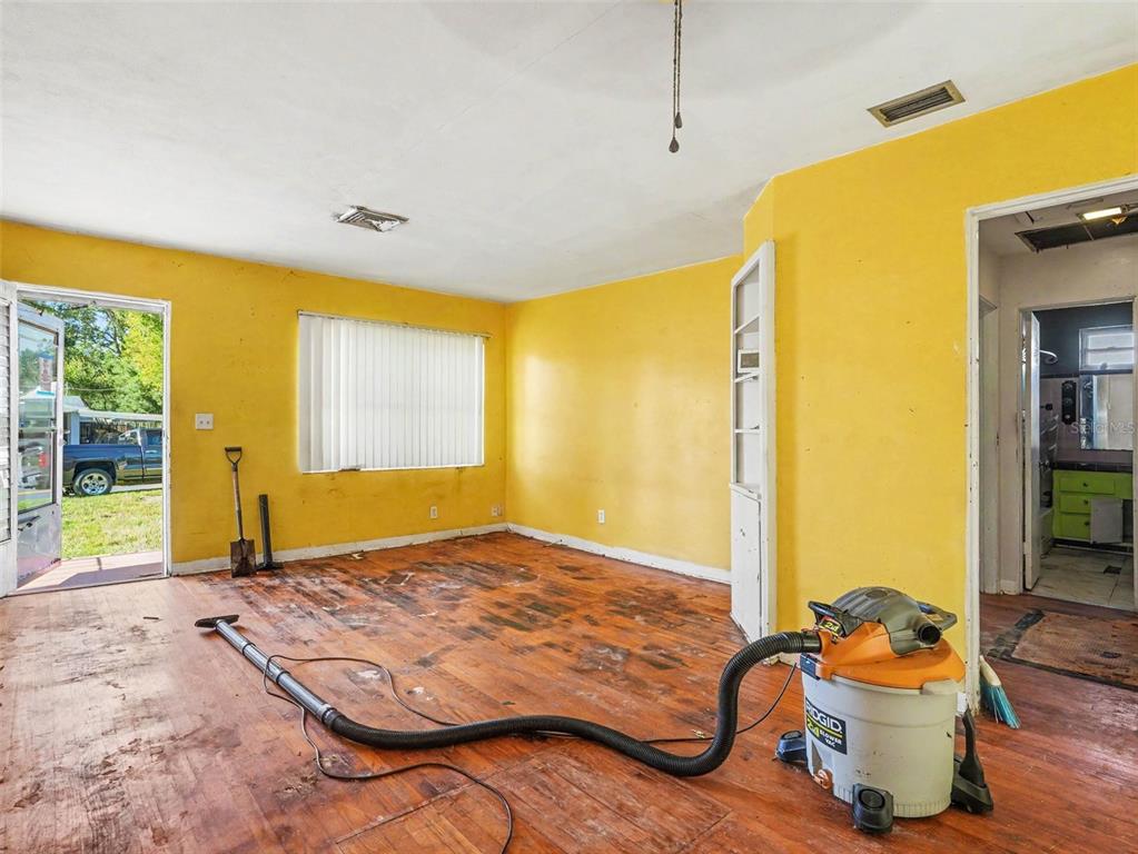 An empty room with yellow walls, a damaged wood floor, and a shop vacuum inside — 2207 AVENUE B NW, WINTER HAVEN, FL