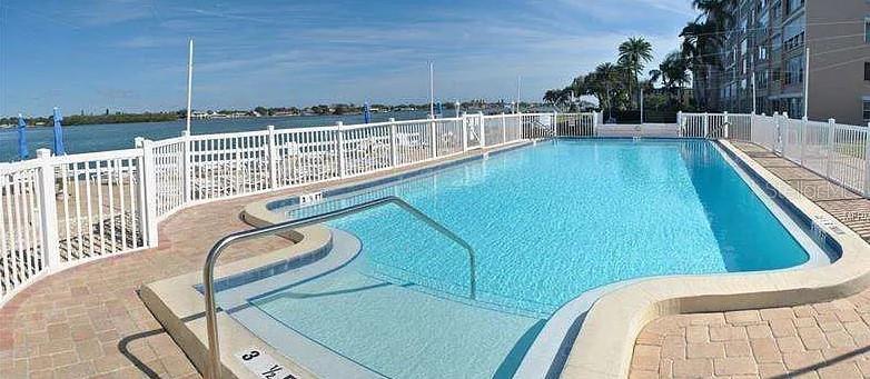 An outdoor swimming pool with a white fence overlooks a body of water — 1819 SHORE DRIVE S UNIT 307, SOUTH PASADENA, FL