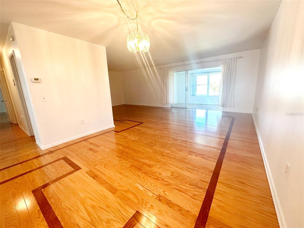 A living room features light hardwood floors with dark wood borders and a glass chandelier — 1819 SHORE DRIVE S UNIT 307, SOUTH PASADENA, FL