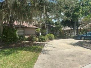 A single-story house with a concrete driveway is surrounded by trees with hanging moss — 2702 CLUBHOUSE DRIVE, PLANT CITY, FL