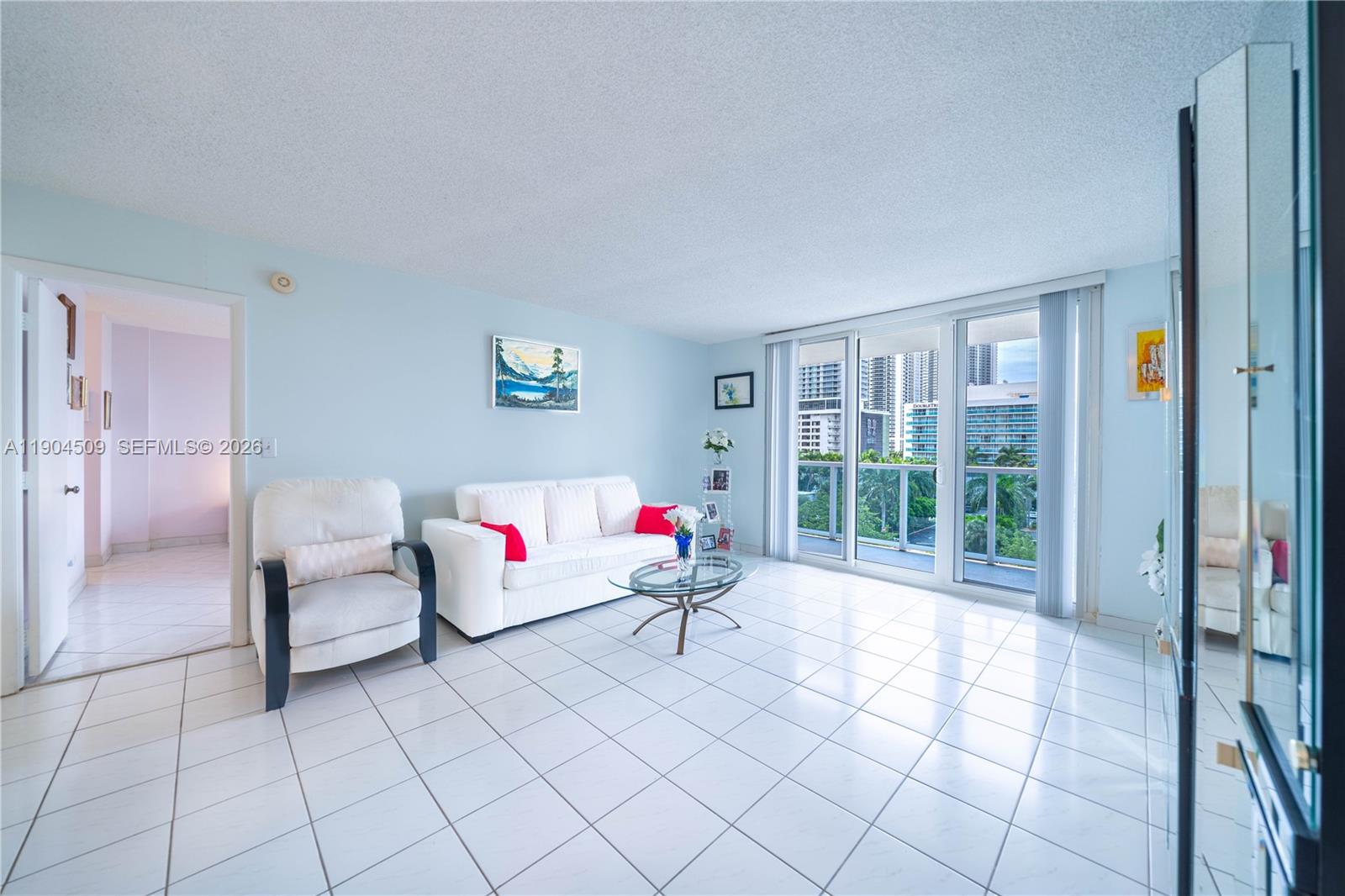 A living room with white tile floors, a white sofa, and a balcony overlooking buildings — 3800 S Ocean Dr, Hollywood FL 33019, HOLLYWOOD, FL