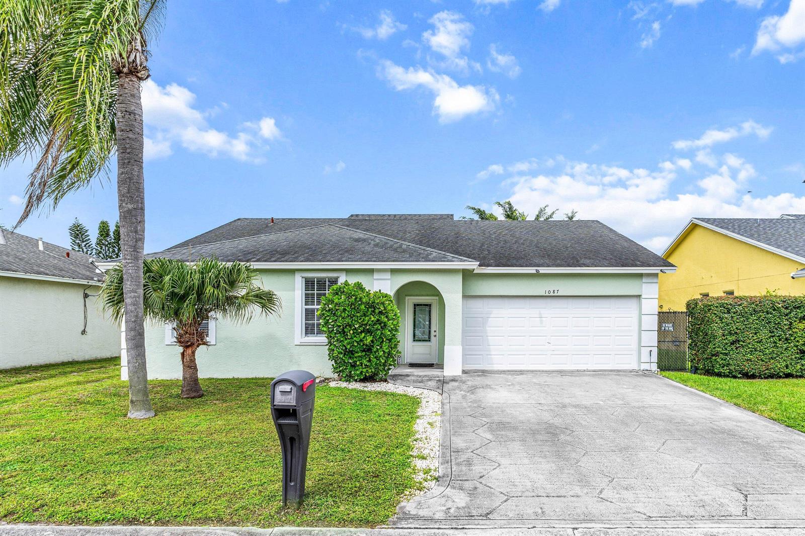 A light green single-story house features a white garage door, a palm tree, and landscaping — 1087 Salmon Isle, FL 33413, FL